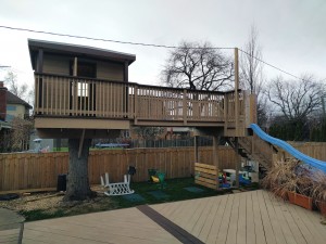The play structure consists of a raised deck and tree fort, with two slides leading into a swimming pool.