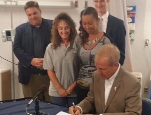 Gov. Bruce Rauner signs the reform bill as Lisa Creason stands behind him. (INN Photo by Ben Yount)