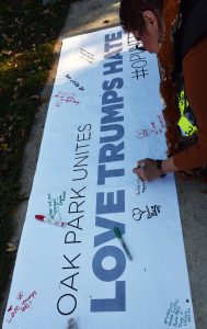 Signing a banner taped to a sidewalk is Maureen Meshenberg of Oak Park. She’s among approximately more than 200 supporters on Nov. 12, 2016 in Oak Park at Scoville Park during the Community for Unity Rally by the Suburban Unity Alliance. (Photo by Karie Angell Luc / for Chronicle Media)