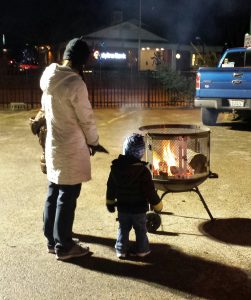 As they waited for Santa to show up at Oswego's Annual Christmas Walk on Friday night Dec. 2, several people warmed themselves by a small fire.  (Photo by Erika Wurst/for Chronicle Media) 